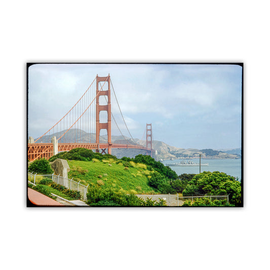 the iconic Golden Gate Bridge spanning across a body of water, with lush greenery and a cloudy sky in the background. Golden Gate Bridge & Warship Vintage Photo – San Francisco Art