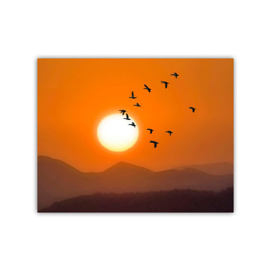 A flock of birds silhouetted against a vibrant orange and yellow sunset sky, with mountains in the distance. Birds in Flight at Sunset Print | Arizona Desert Landscape Art
