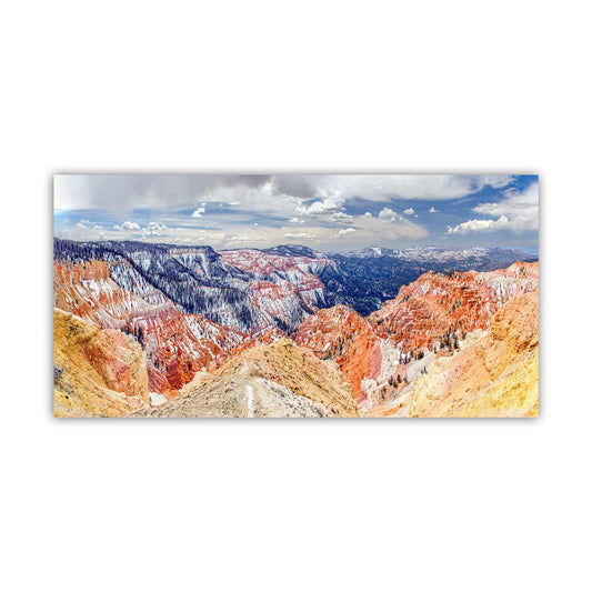A panoramic view of a mountainous landscape with vibrant red and orange rock formations, snow-capped peaks, and a cloudy blue sky. Cedar Breaks Utah National Park Panorama Art Print