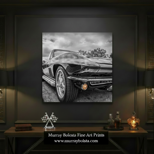 A square black-and-white photo print of a classic car front end, shown centered on a white background with text below stating 'Photo Print Option is sold borderless and unframed'. The depicted scene is monochrome, with the car rendered in black, gray, and white tones; the small amber round light is a minor accent. Vintage Corvette by Murray Bolesta.