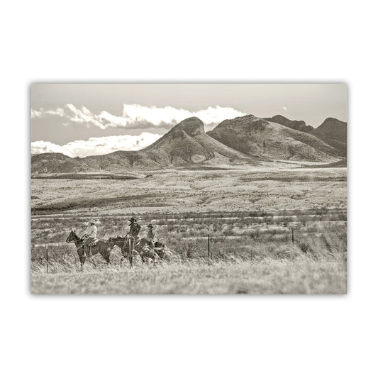 A black and white photograph depicting two cowboys riding horses in a vast, open field with mountains in the distance. Cowboy Art Print Empire Ranch | Western Equestrian Wall Decor
