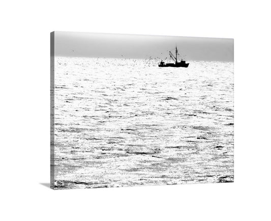 A black and white image of a fishing boat sailing on a calm body of water, with a flock of birds flying in the background. Block Island Fishing Trawler Art Print | Black & White Ocean Photo
