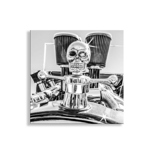 A close-up black and white image of a chrome or metallic object, possibly a part of a vehicle, with a skull-shaped ornament or emblem prominently displayed. Ford Model T Hot Rod Art – Square Format Black & White