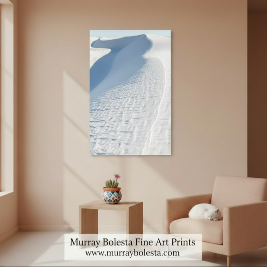 A sand-covered landscape with a large, curving dune in the distance. Minimalist Sand Dune Print - Pale Blue White Sands Photography Art by Murray Bolesta