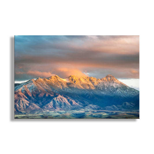 Santa Rita Mountains Tucson Arizona fine art print by Murray Bolesta. A framed landscape art print of snow-capped mountains at sunrise hangs on a beige wall in a styled living room with a sofa, coffee table, chairs, and a golden dog. Text at the bottom reads 'Murray Bolesta Fine Art Prints' with the website below.