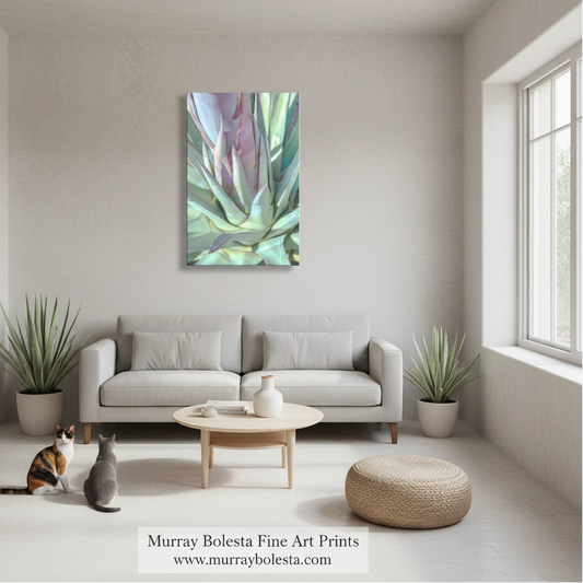 Agave pastel by Murray Bolesta! A framed abstract botanical art print hangs on a light beige wall above a modern light gray sofa in a bright, minimalist living room. The artwork features soft blended tones of green, teal, lavender, and pink.