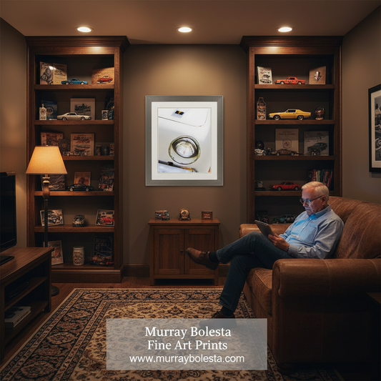 A framed fine art print by Murray Bolesta hangs on a dark brown wall in a cozy, dimly lit home office or living room. The print features a minimalist white background with a circular gold-toned ring.