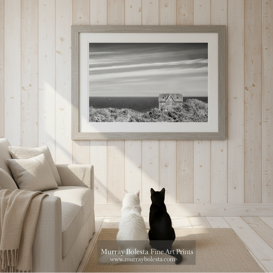 A black and white photograph of a house on a cliff overlooking the ocean, with a sailboat visible in the distance. Block Island Seaside Cottage Fine Art - Black & White Wall Art Print by Murray Bolesta!