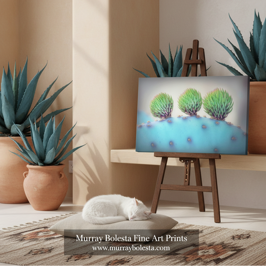 Arizona blue cactus art by Murray Bolesta! A framed-style art print showing three green succulent-like forms on a light blue background, displayed on a wooden easel in a styled interior with potted agaves, a white cat on a rug, and a visible watermark reading Murray Bolesta Fine Art Prints.