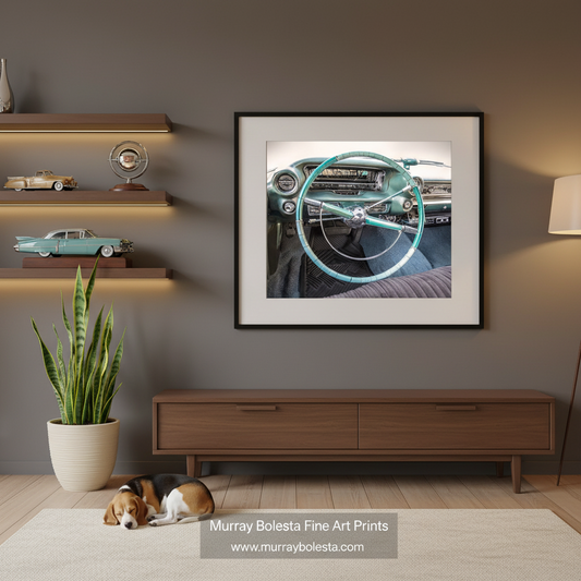 Cadillac art by Murray Bolesta! A framed art print of a vintage car dashboard and steering wheel in teal and black, displayed on a dark gray wall in a modern living room mockup with a wooden console, shelves, and a sleeping dog.