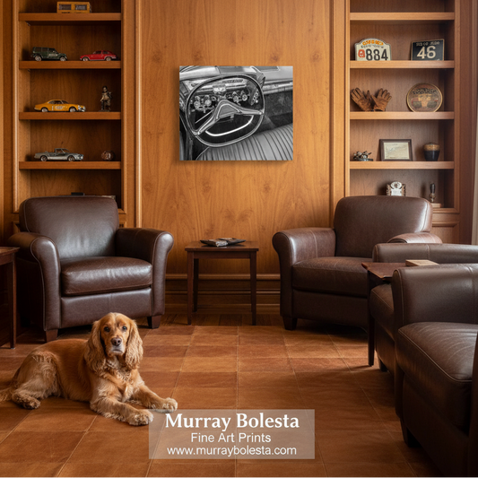 Chrysler Imperial art. A black and white art print of a vintage car dashboard is displayed on a warm wood wall in a cozy living room setting with two brown leather armchairs, a small side table, and a golden dog lying on the floor. A watermark at the bottom reads 'Murray Bolesta Fine Art Prints'.