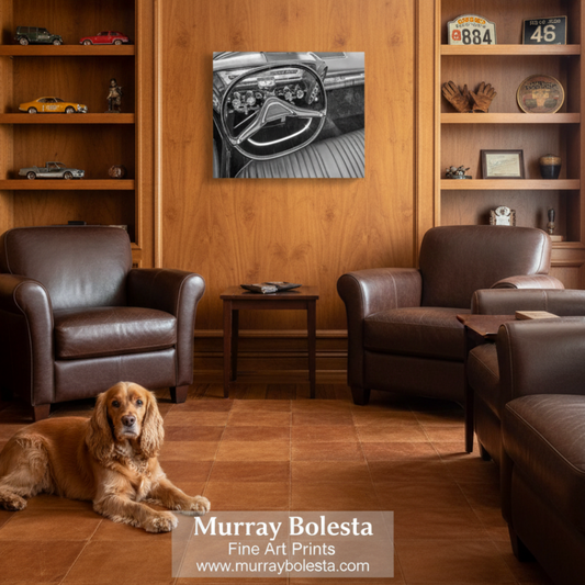 Chrysler Imperial art. A black and white art print of a vintage car dashboard is displayed on a warm wood wall in a cozy living room setting with two brown leather armchairs, a small side table, and a golden dog lying on the floor. A watermark at the bottom reads 'Murray Bolesta Fine Art Prints'.
