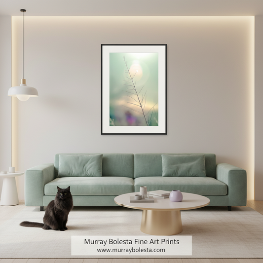 A framed abstract art print featuring a delicate branch silhouette against a soft green and cream background, displayed on a beige wall above a mint green sofa in a modern living room setting. A black cat sits on the floor to the left, and a white text banner at the bottom displays the brand 'Murray Bolesta Fine Art Prints'.