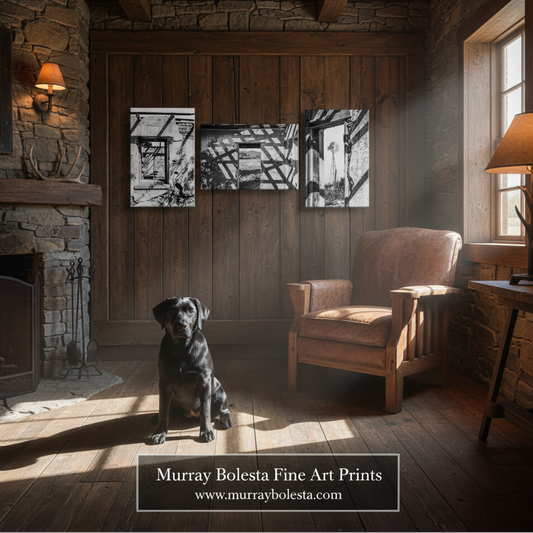 A rustic interior scene with a black dog sitting in the foreground, a wooden chair, stone walls, and three framed black-and-white art prints mounted on the wood-paneled wall. Text at the bottom reads 'Murray Bolesta Fine Art Prints' with the website murraybolesta.