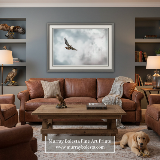 A framed wall art print showing a bird flying through clouds, displayed above a brown leather sofa in a styled living room. A golden retriever lies on the rug in the foreground.