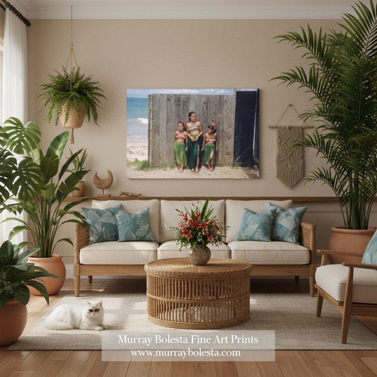 A framed family photograph print hangs on a beige wall above a light wood sofa in a styled living room with plants, a rattan coffee table, and neutral-toned decor. The print shows a family standing in front of a weathered wooden fence near the ocean.