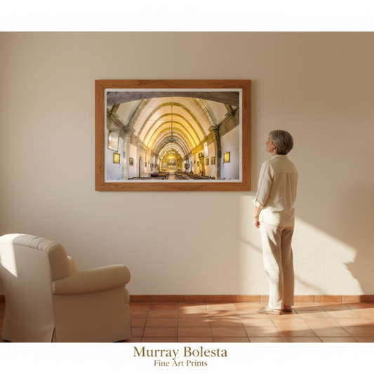 A framed art print depicting a golden archway cathedral interior hangs on a beige wall in a sunlit room, with a person standing in front of it. The text 'Murray Bolesta Fine Art Prints' appears at the bottom.