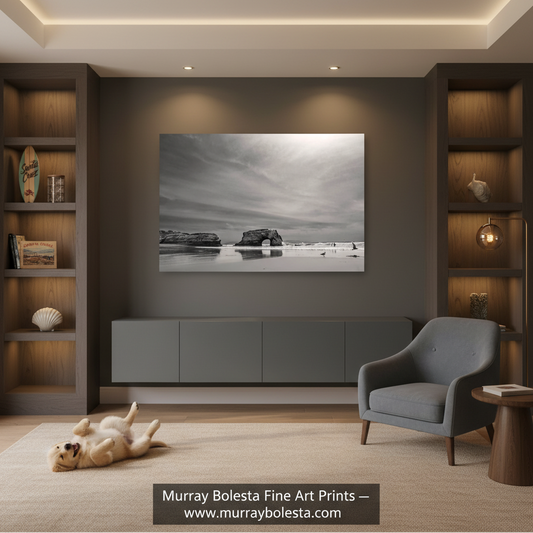 A black and white landscape art print by Murray Bolesta is displayed on a dark gray wall in a modern living room setting with a gray armchair, built-in wooden shelves, and a small dog lying on the carpet.