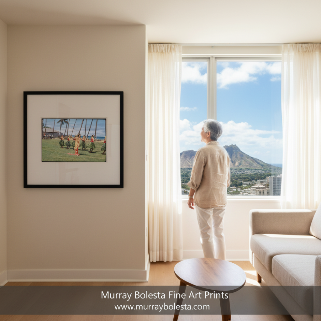 A framed art print depicting a Hawaiian hula dancer on a grassy field is displayed on a beige wall in a modern living room. An elderly woman stands by a large window looking out at a scenic mountain view under a blue sky. by murray bolesta.