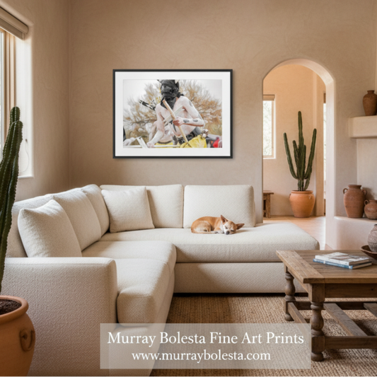 A framed art print by Murray Bolesta hangs on a beige wall in a modern living room setting with a cream sectional sofa, wooden coffee table, and potted cacti.