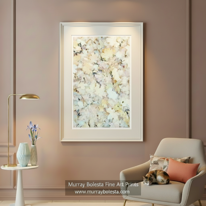 A framed abstract art print with soft cream, beige, and white brushstrokes hangs on a dusty pink wall in a styled living room setting with a modern armchair, side table, and lamp. by Murray Bolesta