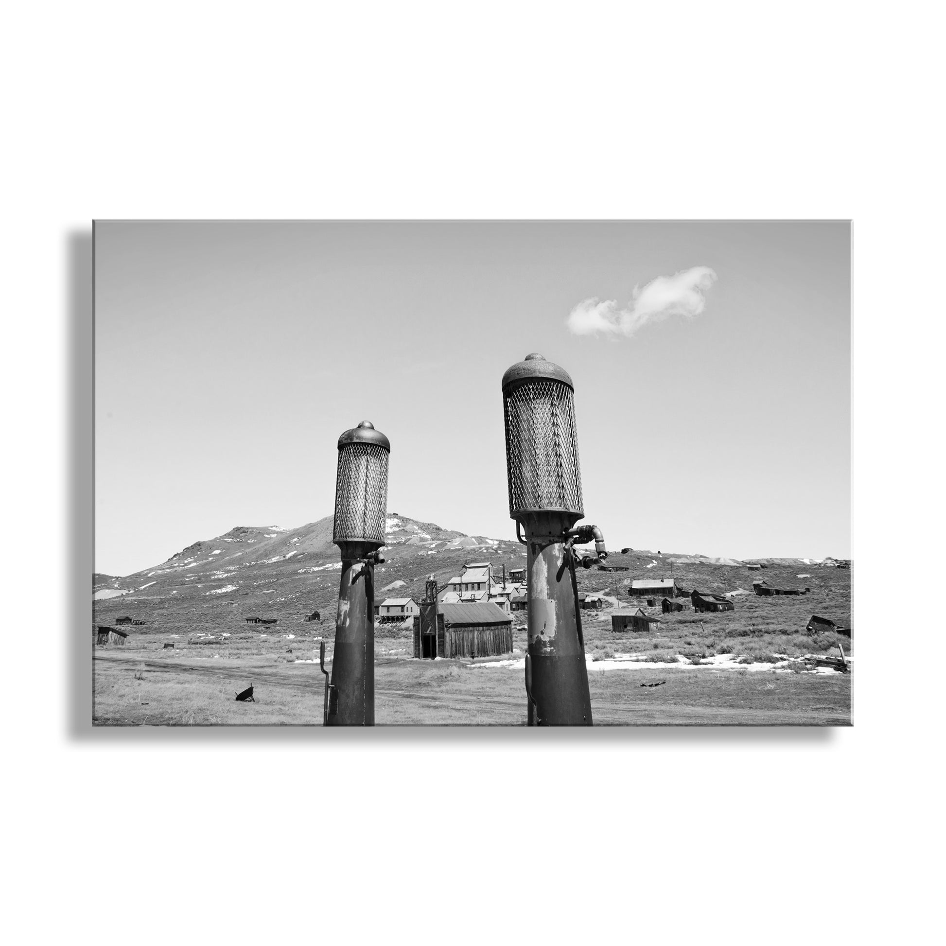 Two cylindrical structures on stilts with a mountainous landscape in the background. Bodie California Ghost Town Art with Vintage Gas Pumps in Black & White