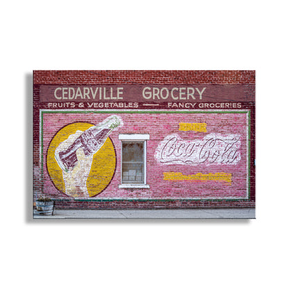 Framed artwork of a vintage Coca-Cola advertisement on a brick wall with 'Cedarville Grocery' text. Vintage Coca Cola Street Sign on Brick Wall in Cedarville California