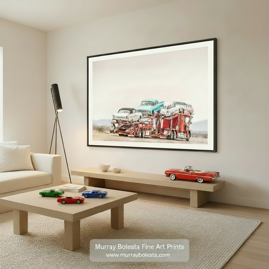 A red and white car carrier is transporting a collection of vintage cars, including a white car, a blue car, and a white car, on a desert road. Road Trip Car Photography – Mid-Century Cars Art Print by Murray Bolesta