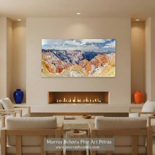 A panoramic view of a mountainous landscape with vibrant red and orange rock formations, snow-capped peaks, and a cloudy blue sky. Cedar Breaks Utah National Park Panorama Art Print by Murray Bolesta