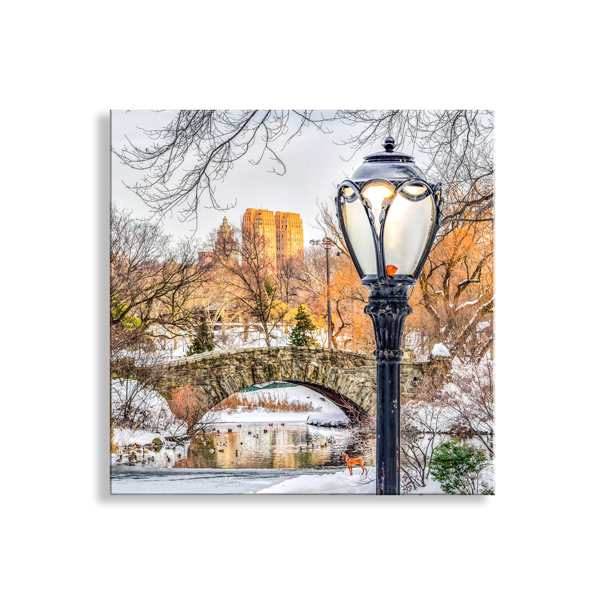 Snowy park scene with a lamp post and bridge in the background. Snowy Winter Central Park Art Print – Gapstow Bridge in NYC