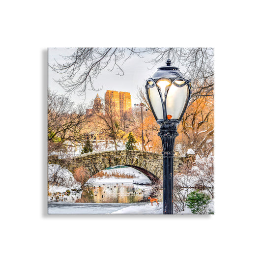 Snowy park scene with a lamp post and bridge in the background. Snowy Winter Central Park Art Print – Gapstow Bridge in NYC
