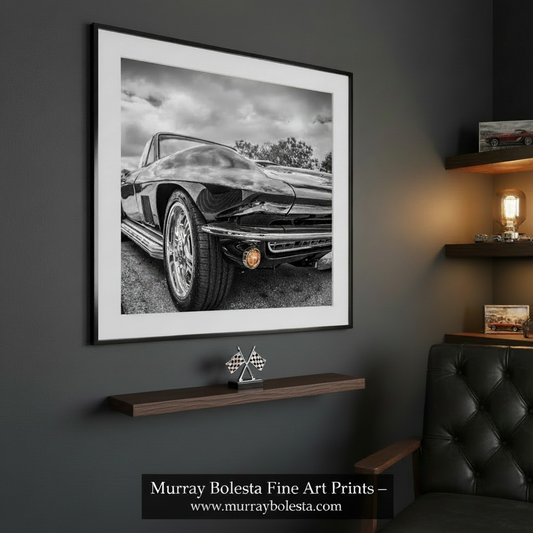 A square black-and-white photo print of a classic car front end, shown centered on a white background with text below stating 'Photo Print Option is sold borderless and unframed'. The depicted scene is monochrome, with the car rendered in black, gray, and white tones; the small amber round light is a minor accent. Corvette art by Murray Bolesta