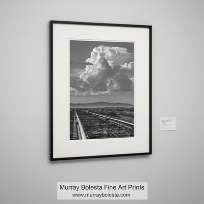 Black and white photograph of a railway track leading towards a large cloud. By Murray Bolesta.