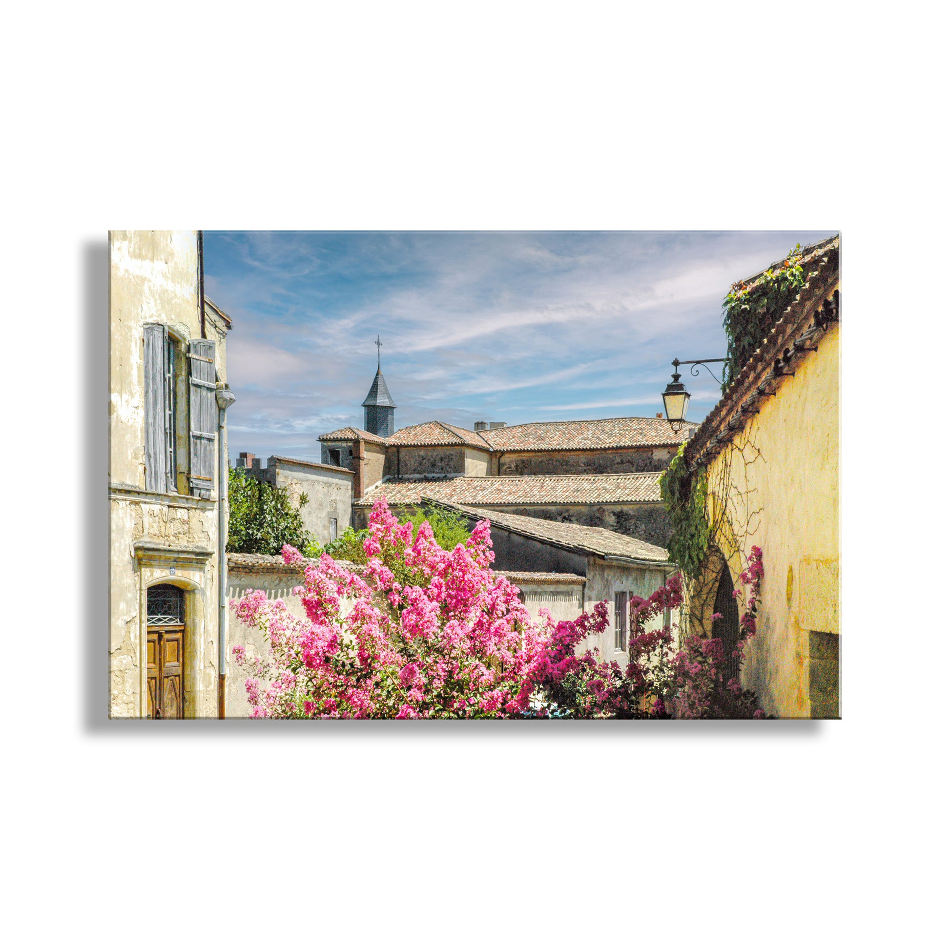 a picturesque European village scene, featuring colorful buildings, a church with a tall spire, and a vibrant flowering bush in the foreground. Quaint French Village Art Print | Vintage France Wall Decor