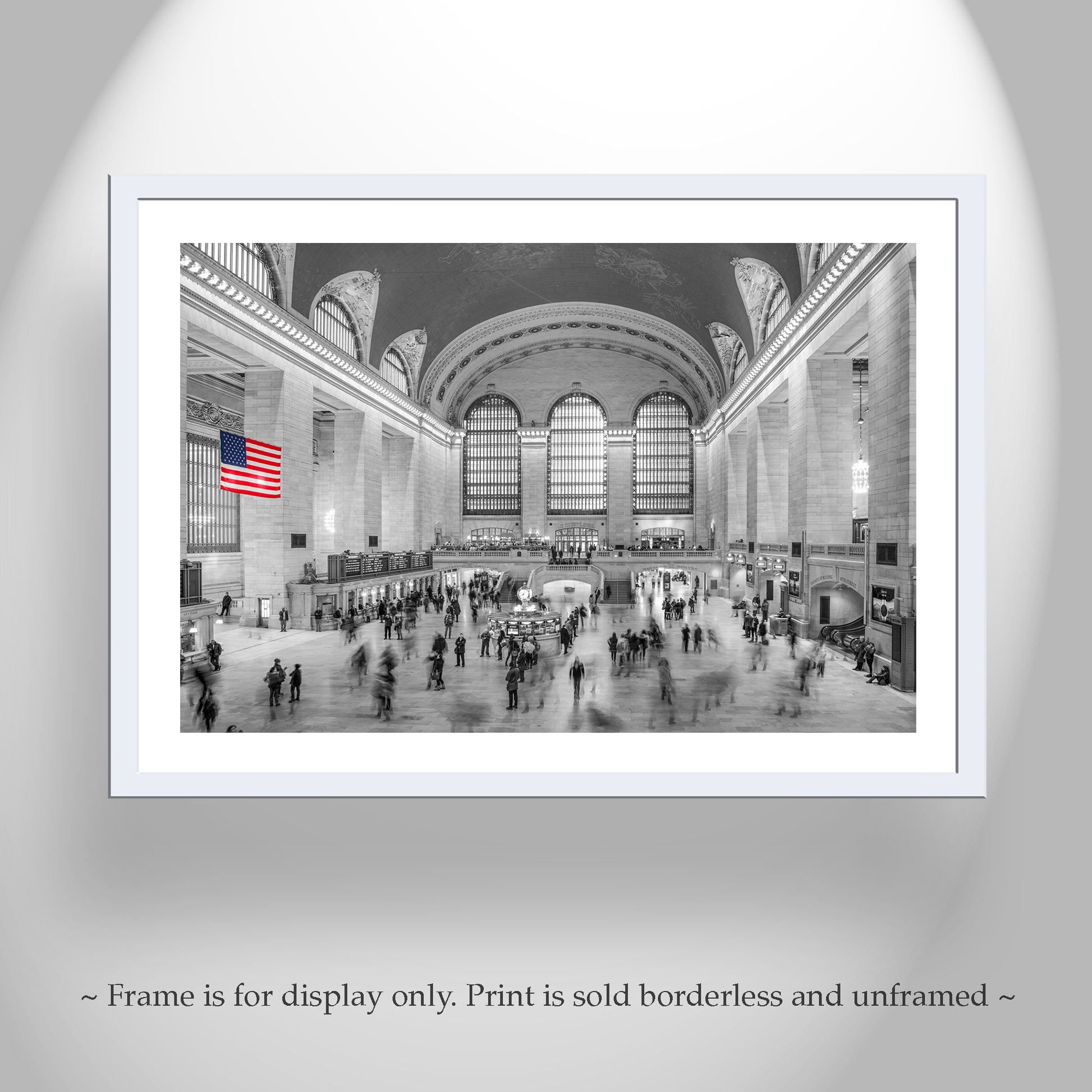 Framed print of a busy train station with an American flag, displayed on a gray wall. Grand Central Terminal New York City Black & White Wall Art Decor