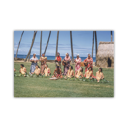 Group of people in traditional attire sitting on grass with palm trees and ocean in the background. Old Hawaii Photo of Hawaiian Islands Hula Dancers & Musicians