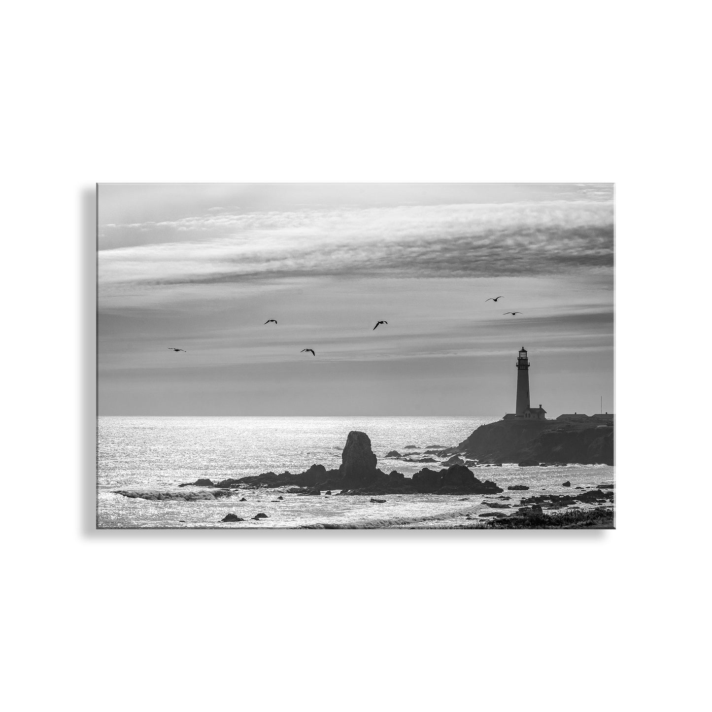 Black and white scene of a lighthouse on a rocky island with birds flying over the ocean. California Lighthouse Wall Art in Black & White at Pigeon Point