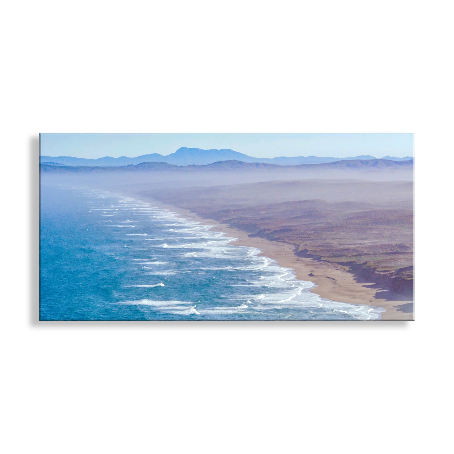 A panoramic landscape art print depicting an aerial view of a coastline with turquoise ocean waves, white surf, a sandy beach, and distant blue mountains under a pale sky, shown hanging against a white wall. My panoramic Point Reyes National Seashore scene at the California coast: an empty beach, almost limitless! An original artwork by Murray Bolesta. Original, unique signed art by Murray Bolesta.&nbsp;