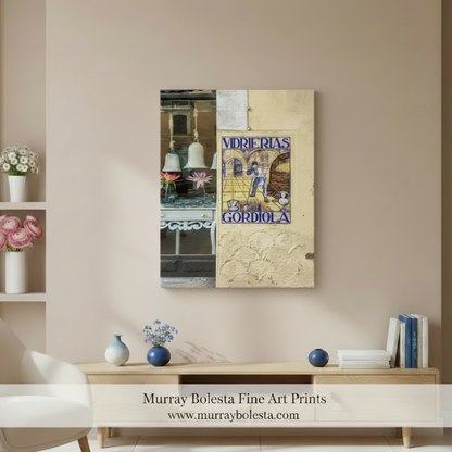 A vertical canvas art print featuring a collage of tiles and street scenes from Goriodela, Spain, displayed on a beige wall in a styled living room mockup. The print has a textured, vintage aesthetic with blue, beige, and brown tones. Murray Bolesta