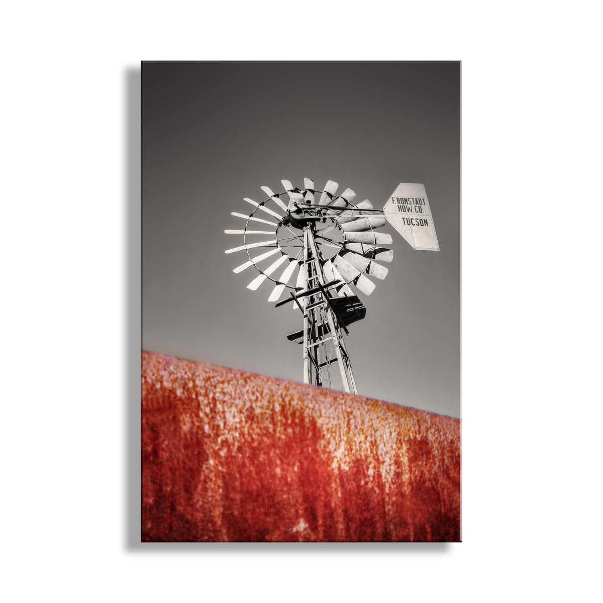 Windmill against a gray sky with a red field below. Vintage Ranch Windmill with Rusty Stock Tank as Arizona Ranch Wall Decor