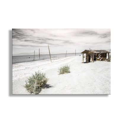 Desert landscape with a small wooden structure and sparse vegetation under a cloudy sky. Salton Sea Lake Art Photograph in Mojave Desert Southern California