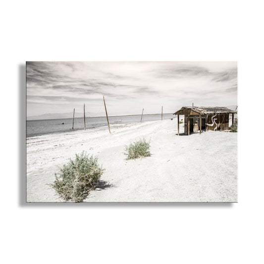 Desert landscape with a small wooden structure and sparse vegetation under a cloudy sky. Salton Sea Lake Art Photograph in Mojave Desert Southern California