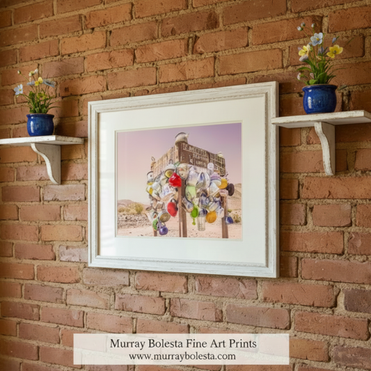 A signpost in a desert-like environment, with various colorful and uniquely shaped objects hanging from it, including pots, bottles, and other containers. Teakettle Junction Art - Death Valley California Desert Print by Murray Bolesta
