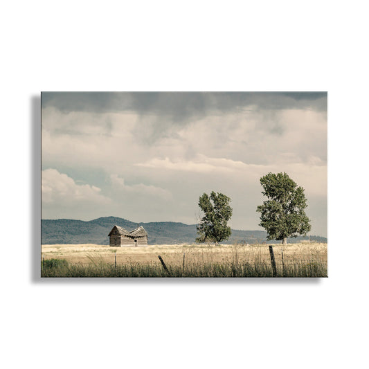 Rural landscape with a small wooden cabin, two trees, and mountains under a cloudy sky. Rustic Country Style Art Print with Western Prairie Landscape & Log Cabin