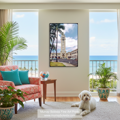 A framed vertical art print depicting a tropical coastal scene with palm trees, a clock tower, and the ocean, displayed on a wall in a bright living room with a pink armchair, plants, and a white dog.