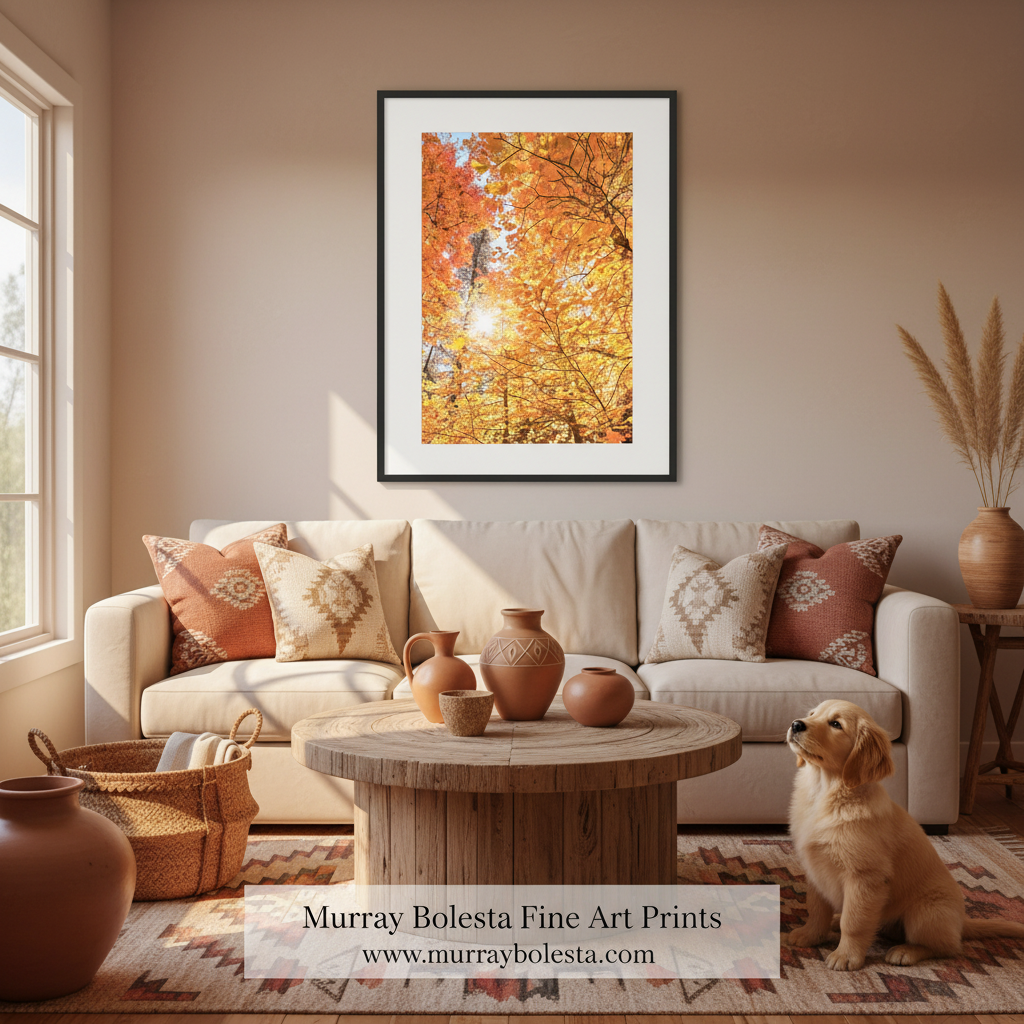 A framed art print of a bright orange autumn forest hangs on a beige wall above a cream sofa in a styled living room. A small golden dog sits on the rug nearby, and a watermark at the bottom reads 'Murray Bolesta Fine Art Prints'.
