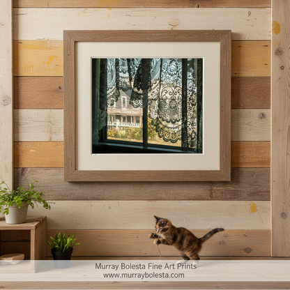 a view through a window with lace curtains, revealing a house and a white picket fence in the background. Block Island cottage by Murray Bolesta!