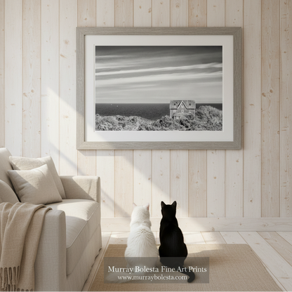 A black and white photograph of a house on a cliff overlooking the ocean, with a sailboat visible in the distance. Block Island Seaside Cottage Fine Art - Black & White Wall Art Print by Murray Bolesta!