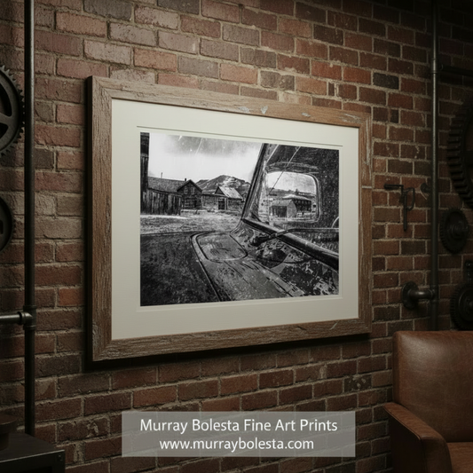 A black and white photograph of a rural landscape, featuring a dilapidated building, a dirt road, and a distant mountain range. Bodie Ghost Town Vintage Truck Art - Black & White Photograph by Murray Bolesta