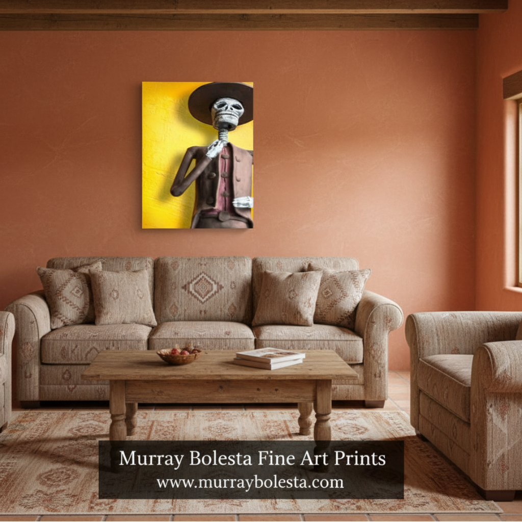 A framed wall art print showing a stylized skeleton figure against a bright yellow background, displayed above a beige sofa in a rustic living room with terracotta walls and wood ceiling beams. Text at the bottom reads 'Murray Bolesta Fine Art Prints' with a website. Day of the Dead.